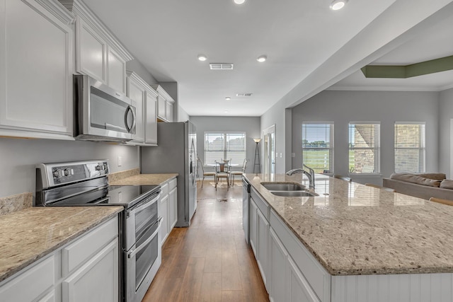 kitchen with a kitchen island with sink, dark wood-type flooring, a sink, visible vents, and appliances with stainless steel finishes