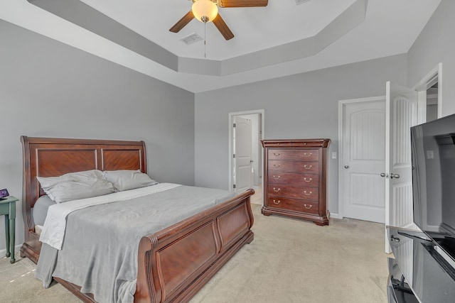 bedroom featuring ceiling fan, light carpet, visible vents, baseboards, and a tray ceiling