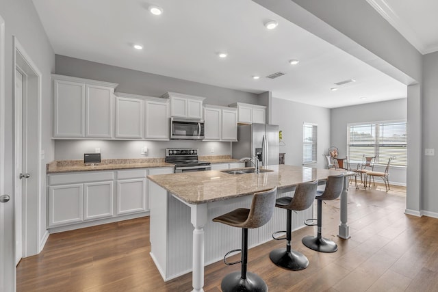 kitchen with a kitchen island with sink, appliances with stainless steel finishes, dark wood finished floors, and a sink