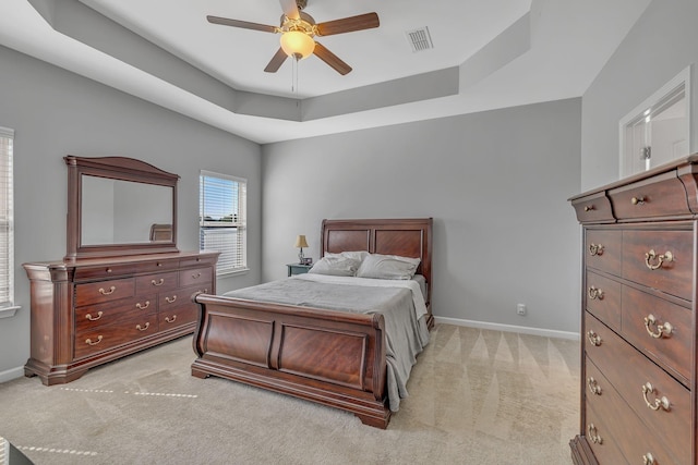 bedroom featuring a raised ceiling, light colored carpet, visible vents, a ceiling fan, and baseboards