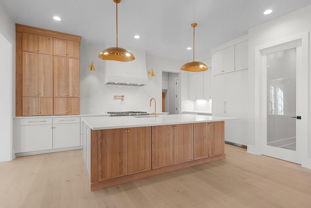 kitchen with light wood finished floors, light countertops, a large island with sink, white cabinets, and a sink