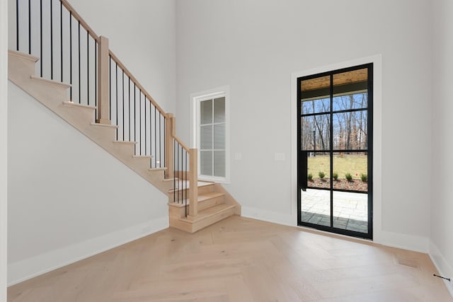 foyer entrance featuring stairway, visible vents, baseboards, and a towering ceiling