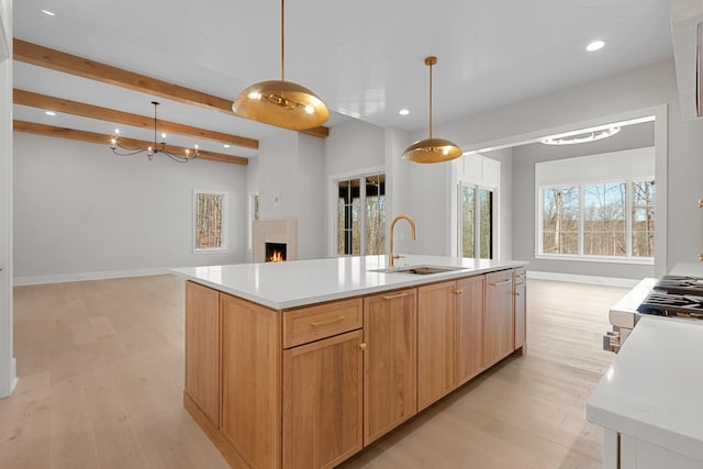 kitchen with light countertops, light wood-style floors, a warm lit fireplace, and a sink