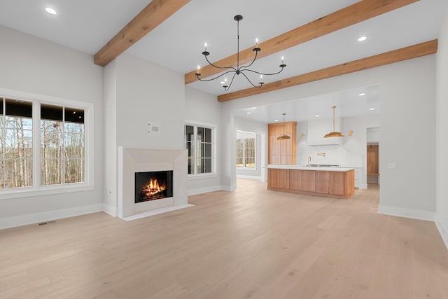 unfurnished living room featuring a wealth of natural light, light wood-type flooring, beam ceiling, and baseboards