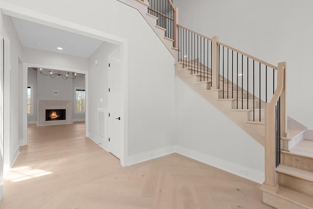 staircase featuring a notable chandelier, recessed lighting, baseboards, and a warm lit fireplace