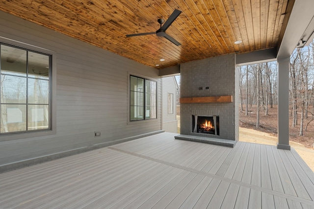 wooden deck with an outdoor brick fireplace and ceiling fan