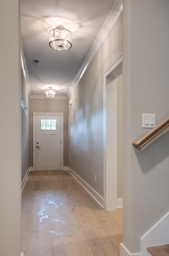 doorway with visible vents, crown molding, baseboards, and wood finished floors