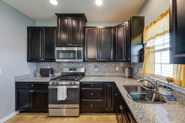 kitchen with decorative backsplash, appliances with stainless steel finishes, a sink, light stone countertops, and baseboards