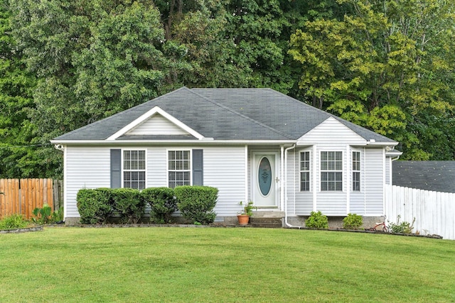 ranch-style house with a shingled roof, fence, and a front lawn