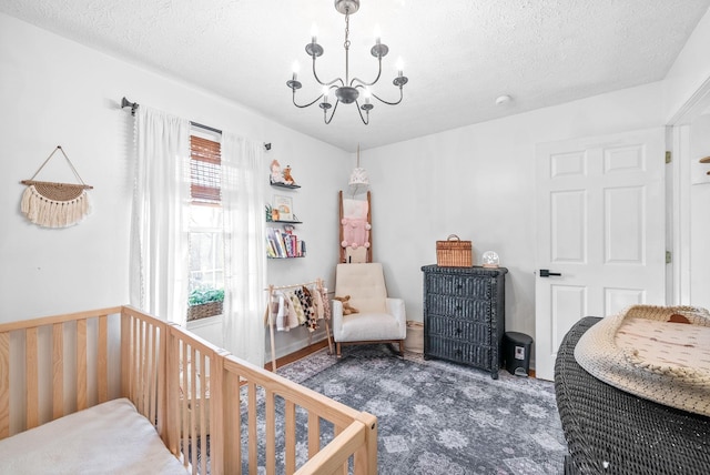 bedroom featuring a nursery area, a notable chandelier, and a textured ceiling