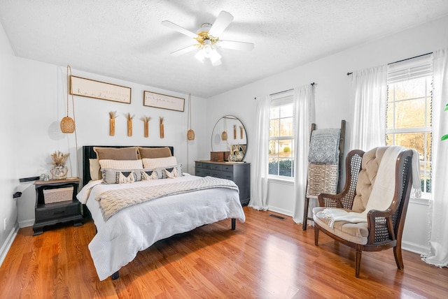 bedroom with a textured ceiling, wood finished floors, visible vents, and baseboards