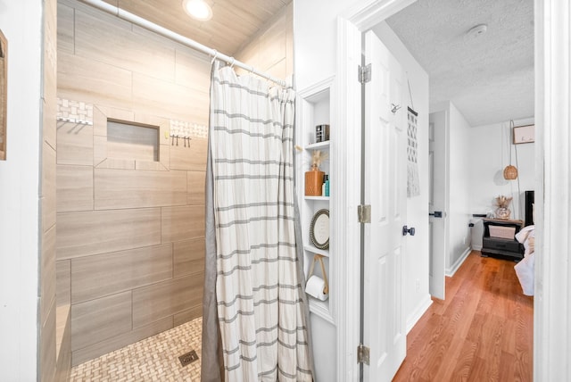 full bath with tiled shower, a textured ceiling, baseboards, and wood finished floors