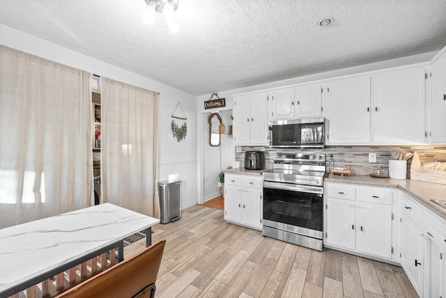 kitchen featuring light wood-style flooring, white cabinets, light countertops, appliances with stainless steel finishes, and tasteful backsplash