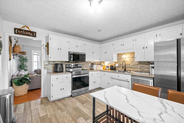 kitchen with light wood-style flooring, appliances with stainless steel finishes, white cabinets, and a sink