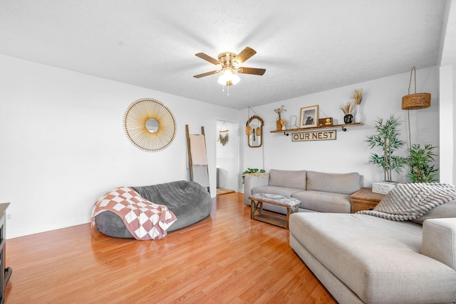 living room featuring light wood-type flooring, ceiling fan, and a textured ceiling