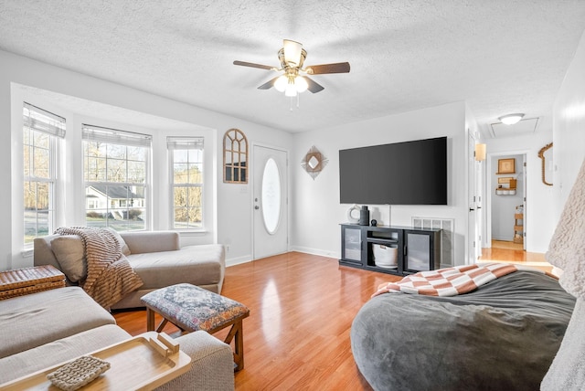 living area with a textured ceiling, ceiling fan, baseboards, and light wood-style floors