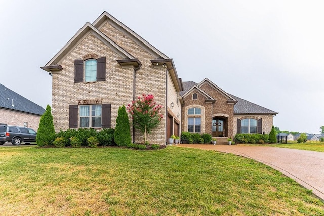 french country style house with decorative driveway, brick siding, and a front lawn