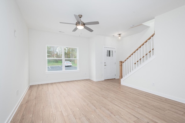 unfurnished living room with a ceiling fan, baseboards, light wood finished floors, and stairs