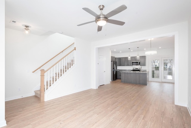 unfurnished living room featuring light wood-style flooring, stairway, and baseboards