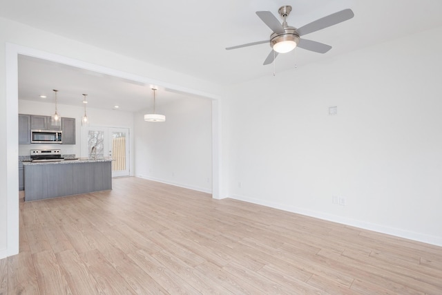 unfurnished living room with light wood-style floors, ceiling fan, baseboards, and a sink