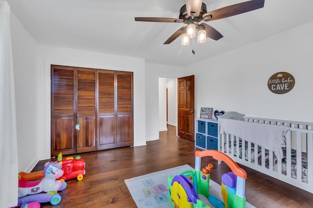 bedroom featuring a crib, baseboards, ceiling fan, wood finished floors, and a closet