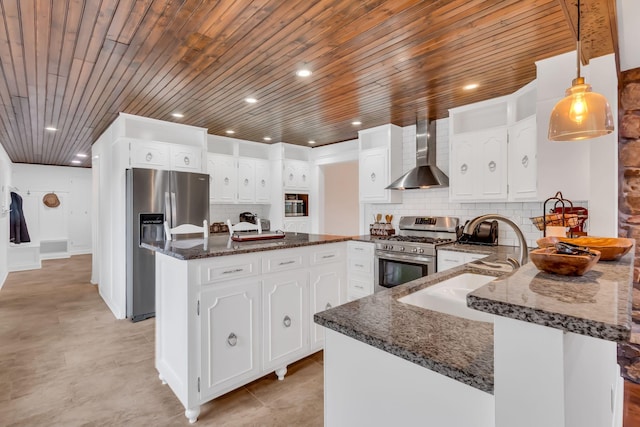 kitchen with a peninsula, appliances with stainless steel finishes, dark stone counters, wall chimney exhaust hood, and tasteful backsplash