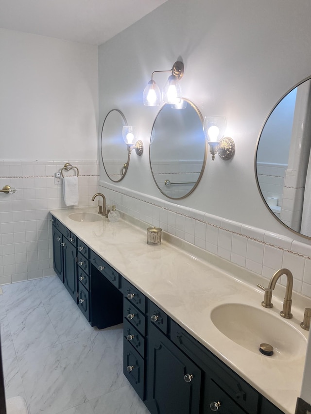 bathroom with marble finish floor, wainscoting, a sink, and double vanity