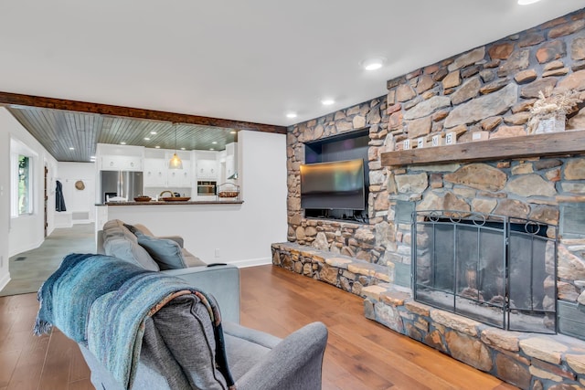 living area with a stone fireplace, beamed ceiling, wood finished floors, and baseboards