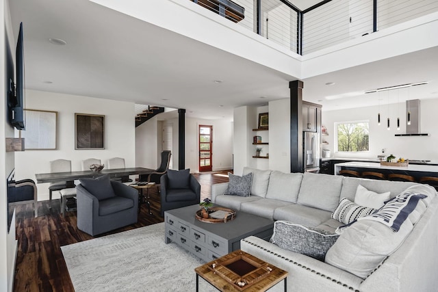 living room with decorative columns, a towering ceiling, baseboards, and wood finished floors