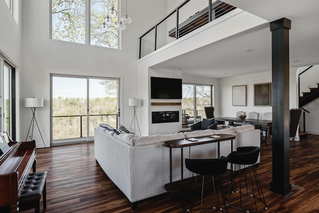 living room featuring a notable chandelier, wood finished floors, baseboards, stairway, and a glass covered fireplace