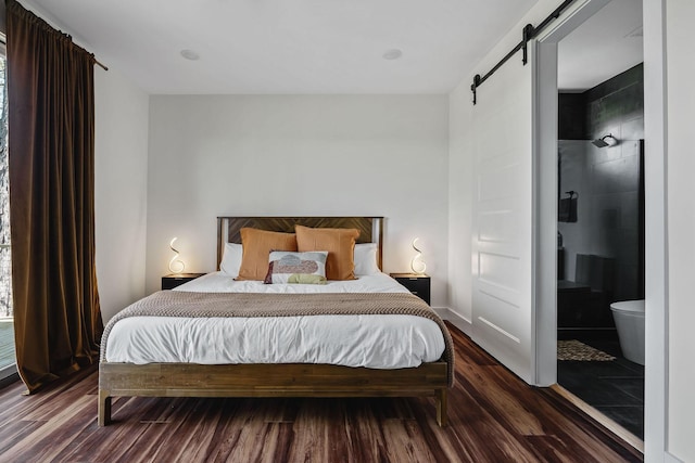 bedroom with ensuite bath, a barn door, and dark wood-style flooring