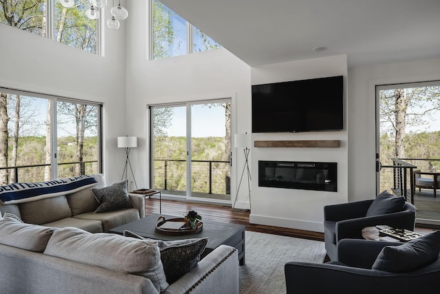 living room with a glass covered fireplace, wood finished floors, and a towering ceiling