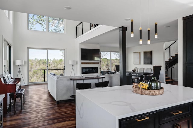 kitchen with open floor plan, dark wood-type flooring, a glass covered fireplace, and light stone counters