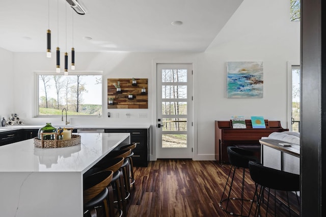 kitchen featuring light stone counters, dark wood-style flooring, a sink, hanging light fixtures, and dark cabinetry