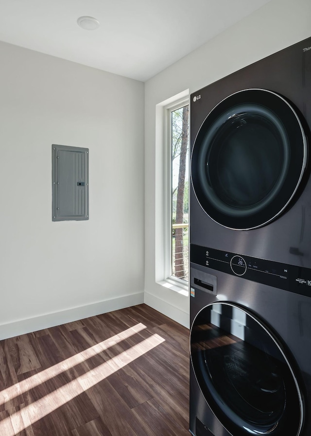 clothes washing area featuring laundry area, electric panel, baseboards, dark wood-style floors, and stacked washing maching and dryer