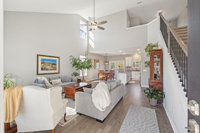 living area with high vaulted ceiling, wood finished floors, a ceiling fan, baseboards, and stairway