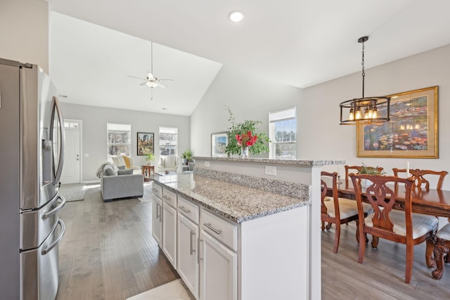 kitchen featuring white cabinetry, a kitchen island, vaulted ceiling, light stone countertops, and stainless steel fridge with ice dispenser