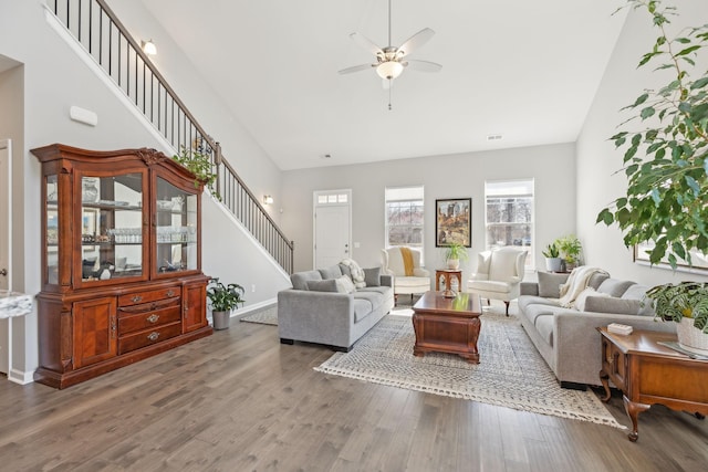 living room with a high ceiling, ceiling fan, wood finished floors, baseboards, and stairs