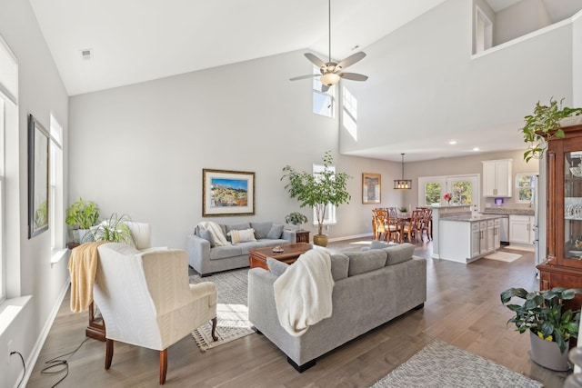 living room with high vaulted ceiling, a ceiling fan, visible vents, baseboards, and dark wood-style floors