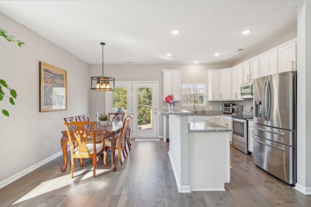 kitchen with dark wood-style floors, appliances with stainless steel finishes, light stone countertops, and white cabinets