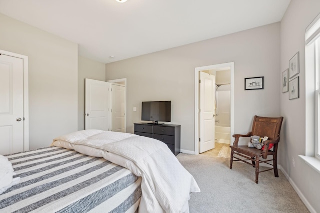 bedroom with light carpet, ensuite bath, and baseboards