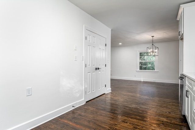 spare room featuring a chandelier, dark wood-style flooring, ornamental molding, and baseboards