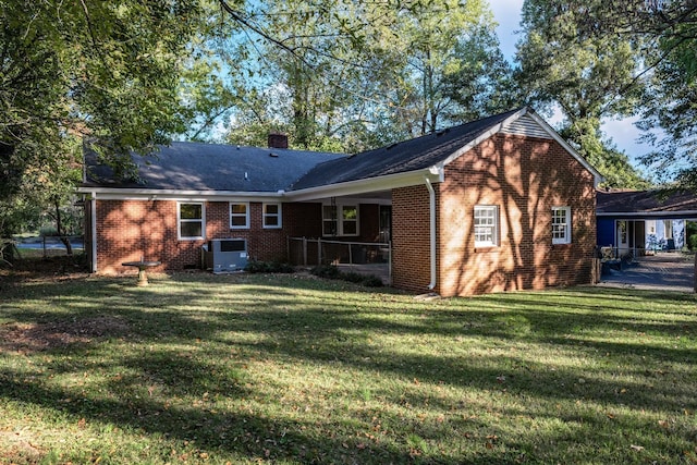 back of house with a carport, brick siding, a lawn, and a chimney