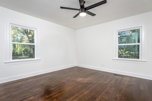 empty room featuring dark wood-type flooring, a ceiling fan, visible vents, and baseboards