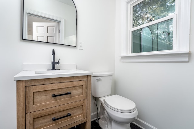 half bath with toilet, baseboards, and vanity