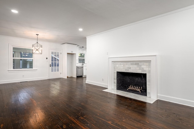 unfurnished living room featuring baseboards, dark wood-style floors, ornamental molding, a brick fireplace, and recessed lighting