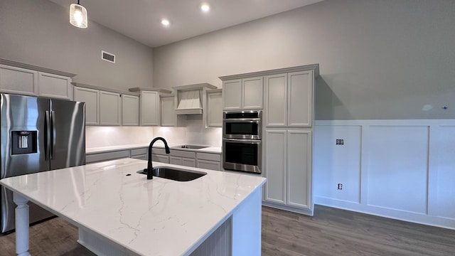 kitchen with a center island with sink, stainless steel appliances, visible vents, a sink, and light stone countertops