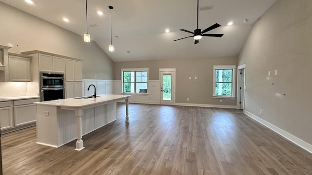 kitchen with stainless steel double oven, open floor plan, a kitchen island with sink, a sink, and a healthy amount of sunlight