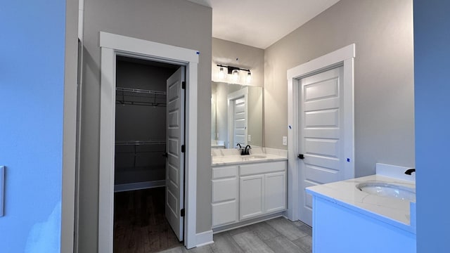 bathroom with a sink, two vanities, a walk in closet, and wood tiled floor