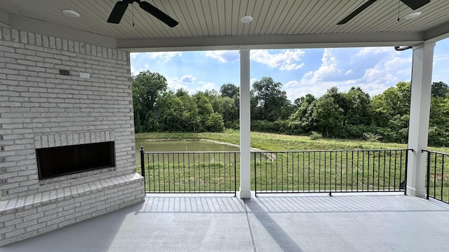 view of patio with a water view, ceiling fan, and an outdoor brick fireplace